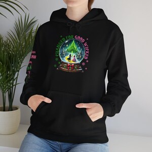 Pode incluir: Hoodie preto com um gráfico de globo de neve verde e rosa que diz "Changed for Good Wicked".