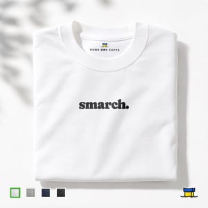 Op de afbeelding: Een gevouwen witte sweatshirt met het woord "smarch." in zwart gecentreerd. De merknaam "BONE DRY CUFFS" is boven de kraag gedrukt. Het ontwerp is minimalistisch, met de nadruk op typografie en de schone witte stof.