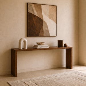 May include: A rectangular wooden console table with a dark brown finish. On top sits a white arched sculpture, a stack of two books, a shallow bowl, a dark brown cylindrical ribbed vase, and a small dark brown sphere. A square abstract painting hangs above.