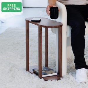 May include: A dark brown, wooden side table with a unique, curved design. The table has a long, oval top and a lower shelf. A smartphone rests on the top surface. The table is 30 inches tall.