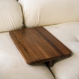 May include: A wooden tray with a natural wood finish sits on a white tufted couch. The tray is rectangular and has a slightly angled edge.