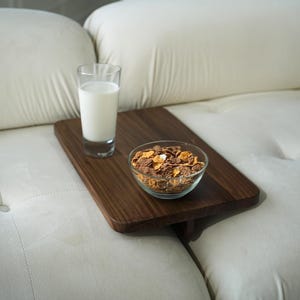 Puede incluir: Una bandeja de madera con un tazón de cereal y un vaso de leche en un sofá blanco. La bandeja está diseñada para ser utilizada en un sofá o cama.