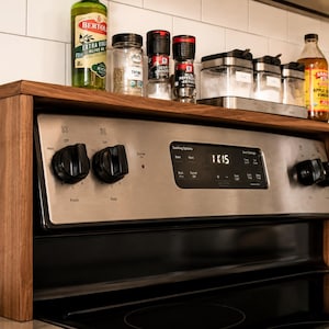 Custom walnut kitchen storage shelf designed to sit above the stove back panel and provide space for spices oils vinegar jars and small decor a practical wooden organizer for a cleaner more organized cooking area