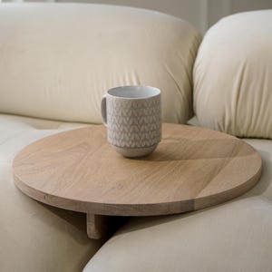 May include: A round wooden tray with a gray ceramic mug with a white pattern on it. The tray is attached to a white couch.