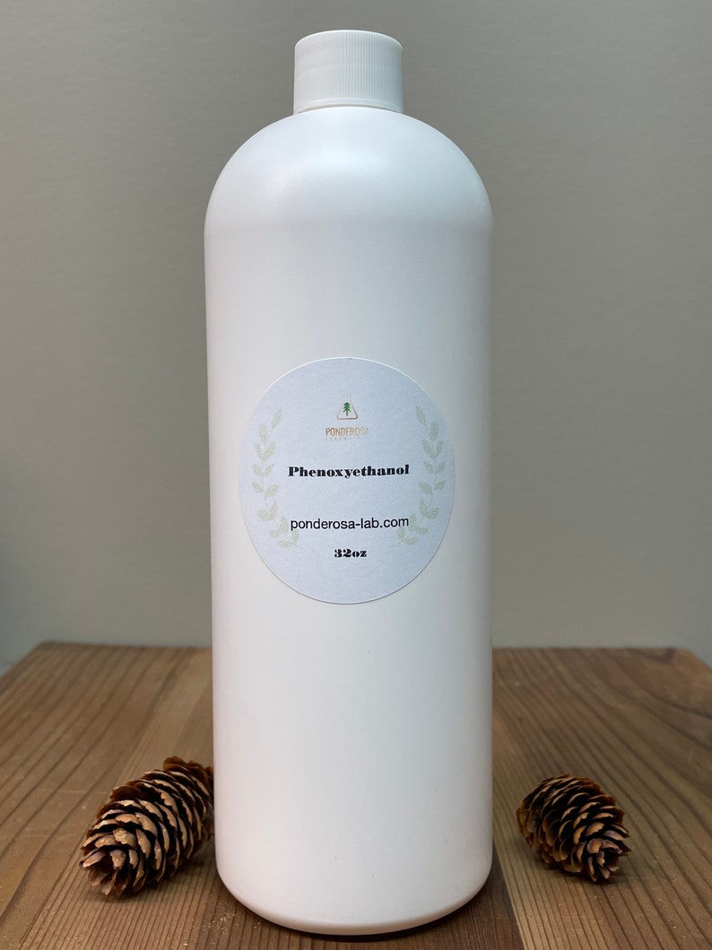 May include: A white plastic bottle with a white label that says "Phenoxyethanol" and "ponderosa-lab.com". The bottle is 32 oz and is sitting on a wooden surface.