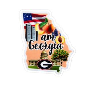 May include: A sticker in the shape of the state of Georgia, with the text "I am Georgia." The design incorporates an American flag, peaches, the state capitol building, and the University of Georgia "G" logo.