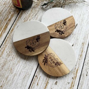 Pu&ograve; includere: Set di tre sottobicchieri rotondi in legno con piano in marmo bianco. Ogni sottobicchiere presenta un design a cuore geometrico con iniziali e una data incisa nel legno. I sottobicchieri sono perfetti per proteggere le superfici dal calore e dagli schizzi.