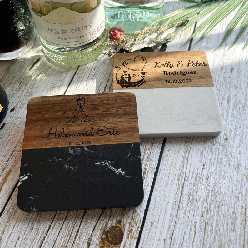 Pu&ograve; includere: Due sottobicchieri in legno con incisioni personalizzate. Il primo sottobicchiere &egrave; in legno chiaro con un top in marmo bianco e presenta il testo "Kelly & Peter Rodriguez 16.10.2023". Il secondo sottobicchiere &egrave; in legno scuro con un top in marmo nero e presenta il testo "Helen and Eric Est. 23.10.23".