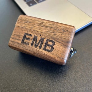 Puede incluir: Una peque&ntilde;a caja de madera con tapa con bisagras y un lazo de metal. La caja est&aacute; hecha de madera oscura con un patr&oacute;n de veta natural. Las iniciales "EMB" est&aacute;n grabadas en la parte superior de la caja.