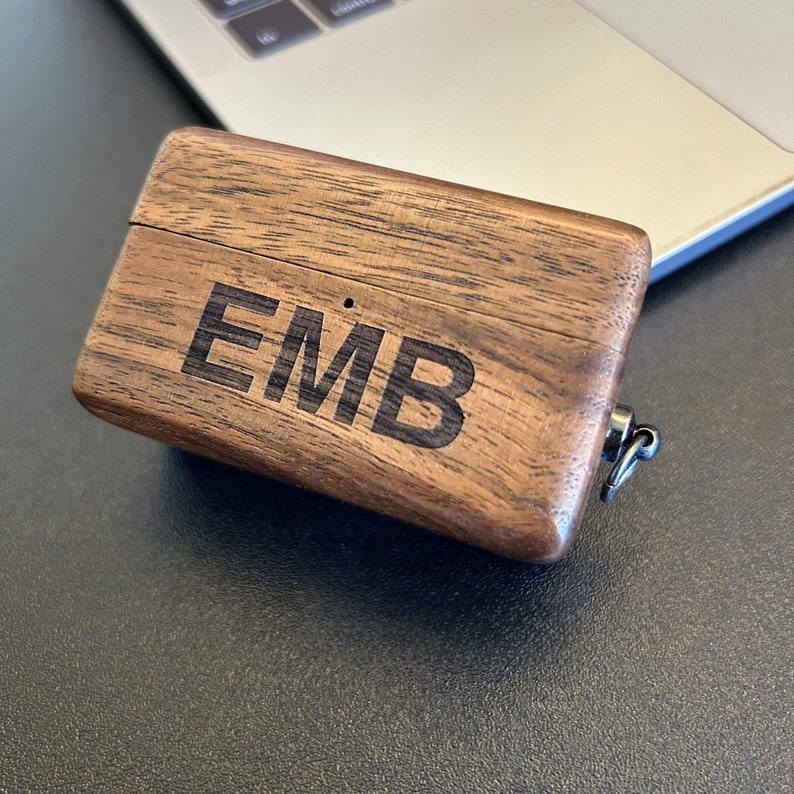 Puede incluir: Una peque&ntilde;a caja de madera con tapa con bisagras y un lazo de metal. La caja est&aacute; hecha de madera oscura con un patr&oacute;n de veta natural. Las iniciales "EMB" est&aacute;n grabadas en la parte superior de la caja.