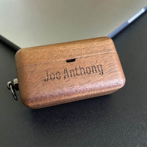 Puede incluir: Una caja de madera personalizada con un lazo de metal para llevar. La caja está grabada con el nombre "Joe Anthony".