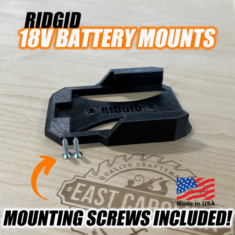 Może przedstawiać: Czarny plastikowy uchwyt do baterii 18V do narzędzi RIDGID. Uchwyt zawiera dwa śruby montażowe. "RIDGID" jest nadrukowane na uchwycie. "Made in USA" jest nadrukowane na naklejce.