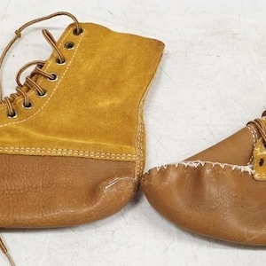 May include: A pair of ankle-high boots featuring a combination of smooth brown leather on the lower section and textured mustard yellow suede on the upper section. The boots include brown laces, metal eyelets, and white whipstitch detailing.
