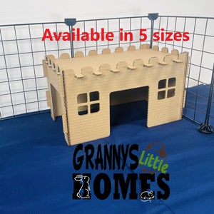 May include: A cardboard castle-shaped pet house with a small entrance and windows. The house is sitting inside a black wire cage. The text "Available in 5 sizes" is written above the house. The text "Grannys Little Homes" is written below the house.