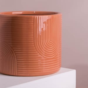 Op de afbeelding: Een terracottakleurige keramische plantenpot met een geometrisch ontwerp. De pot heeft een gladde, glanzende afwerking en een afgeronde vorm.