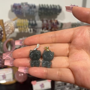 Pode incluir: Dois pingentes de gato de jade verde com correntes de ouro e prata. Os pingentes de gato estão em uma mão.