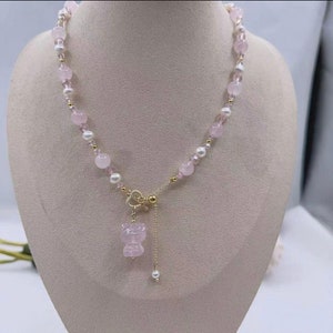 Puede incluir: Un delicado collar de cuentas rosas y blancas con un colgante de piedra rosa. El collar tiene un cierre dorado y un pequeño encanto de perla.