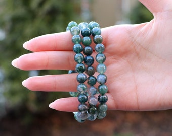 May include: Three green agate beaded bracelets stacked on top of each other. The beads are round and have a mottled green and white pattern.