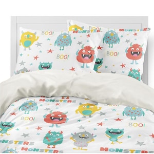 Könnte beinhalten: Ein weißer Bettbezug mit einem sich wiederholenden Muster aus bunten Monstern und Sternen. Der Bettbezug hat die Worte "BOO!" und "MONSTERS" aufgedruckt. Der Bettbezug wird mit zwei Kissenbezügen mit einem ähnlichen Muster geliefert.