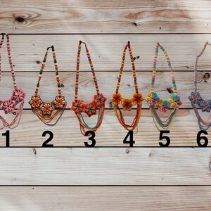 May include: Six colourful crocheted necklaces with flower designs. The necklaces are displayed on a wooden background and numbered 1 through 6.