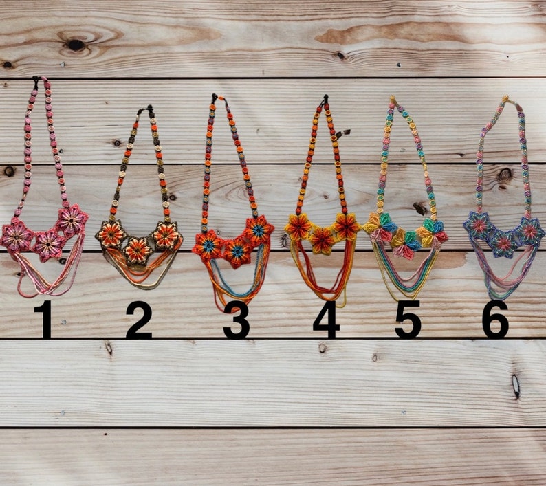 May include: Six colourful crocheted necklaces with flower designs. The necklaces are displayed on a wooden background and numbered 1 through 6.