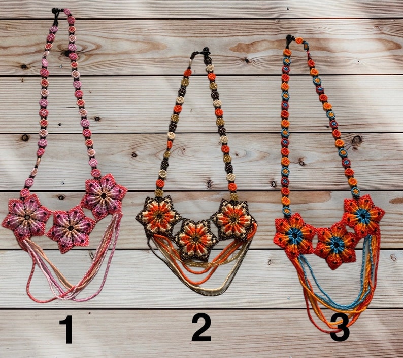 May include: Three beaded necklaces with flower designs. The first necklace is pink and white, the second is orange and brown, and the third is blue, orange, and red. The necklaces are numbered 1, 2, and 3.