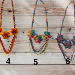 May include: Three beaded necklaces with colourful flower accents. The necklaces are made of multi-coloured beads and feature a layered design. The flowers are made of smaller beads and are arranged in a circular pattern. The necklaces are numbered 4, 5, and 6.