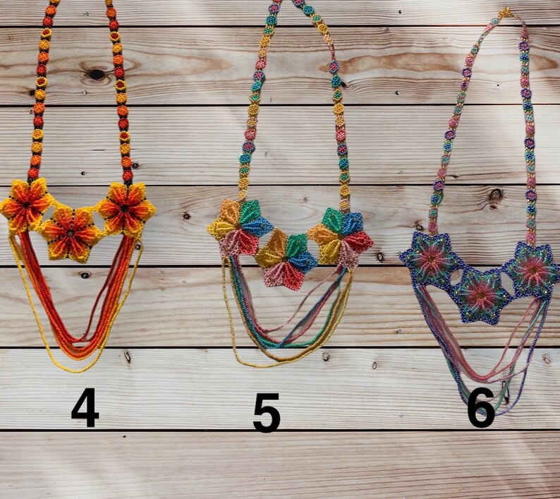 May include: Three beaded necklaces with colourful flower accents. The necklaces are made of multi-coloured beads and feature a layered design. The flowers are made of smaller beads and are arranged in a circular pattern. The necklaces are numbered 4, 5, and 6.