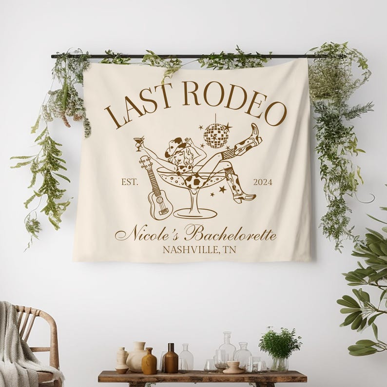 Pu&ograve; includere: Un arazzo beige con testo marrone che recita "Last Rodeo Est. 2024" e "Nicole's Bachelorette Nashville, TN". Un'illustrazione di cartone animato di una donna con un cappello da cowboy e stivali seduta in un bicchiere da martini con un ukulele e una palla da discoteca.