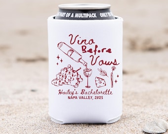 May include: White can cooler with the text "Vino Before Vows" and a wine-themed illustration in burgundy. The text "Hailey's Bachelorette Napa Valley, 2025" is also printed on the cooler. The cooler is on a sandy surface.