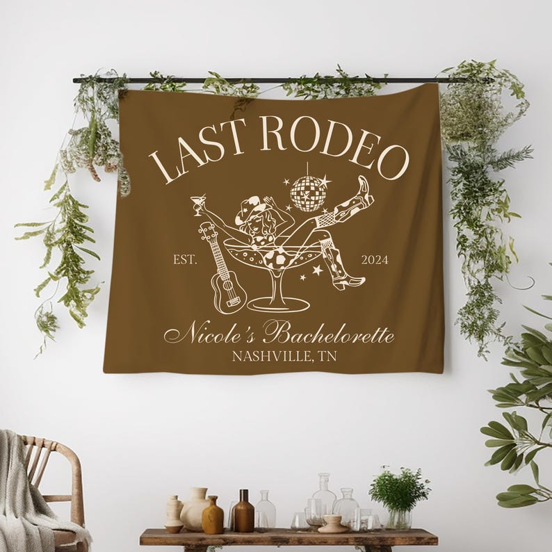 Pu&ograve; includere: Un arazzo marrone con il testo "Last Rodeo" in bianco. L'arazzo presenta una silhouette bianca di una donna con un cappello da cowboy seduta in un bicchiere da martini con una palla da discoteca e un ukulele. Il testo "Est. 2024" e "Nicole's Bachelorette Nashville, TN" &egrave; anche in bianco.