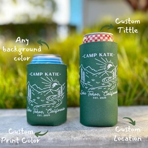 May include: Two green and white insulated can coolers with a mountain scene and the text "Camp Katie - Lake Tahoe, California - Est. 2025". The text "Custom Tittle" and "Custom Location" are written on the image.