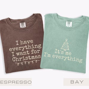 May include: Two Comfort Colors t-shirts, one in espresso brown and one in bay green. The brown shirt reads "I have everything I want for Christmas". The green shirt says "It's me I'm everything".