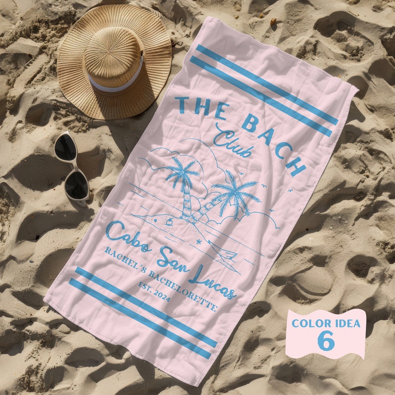 May include: Pink beach towel with blue text that reads "The Bach Club" and "Cabo San Lucas Rachel's Bachelorette Est. 2024". The towel also features a blue illustration of palm trees and a beach scene.