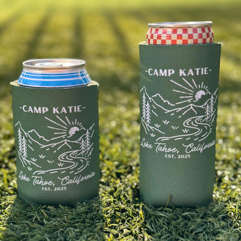 May include: Two green can coolers with a white mountain scene and the text "Camp Katie - Lake Tahoe, California EST. 2025".