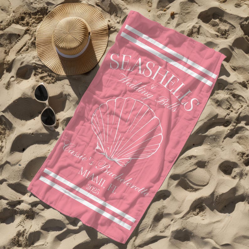 May include: Pink beach towel with white stripes and the text "Seashells & Wedding Bells Cassie's Bachelorette Miami, FL 2023" and a white seashell graphic.