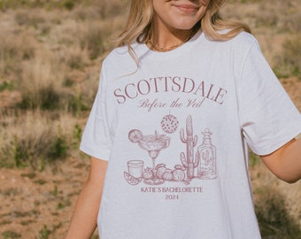 Könnte beinhalten: Weißes T-Shirt mit einem rosafarbenen Grafikdesign, auf dem "Scottsdale Before the Veil" steht und eine Margarita, einen Kaktus und eine Tequilaflasche abgebildet sind. Der Text "Katie's Bachelorette 2024" ist ebenfalls auf dem Shirt zu sehen.