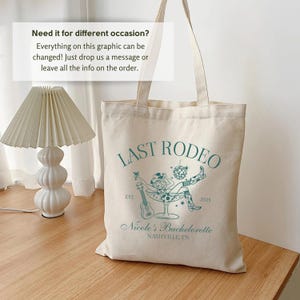 Op de afbeelding: Een beige canvas draagtas met een groen grafisch ontwerp met de tekst "Last Rodeo" met een vrouw in een cowboyhoed die in een martini-glas zit. De grafiek bevat ook de tekst "Est. 2025" en "Nicole's Bachelorette Nashville, TN".