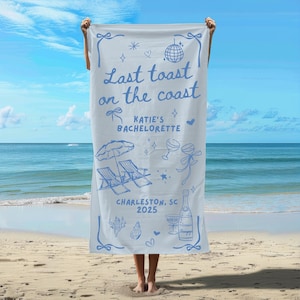 May include: A blue and white beach towel with the text "Last toast on the coast" and "Katie's Bachelorette" with a champagne bottle, glasses, and beach chairs. The text "Charleston, SC 2025" is also on the towel.