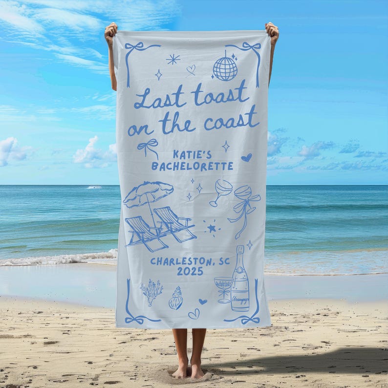 May include: A blue and white beach towel with the text "Last toast on the coast" and "Katie's Bachelorette" with a champagne bottle, glasses, and beach chairs. The text "Charleston, SC 2025" is also on the towel.