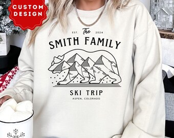 Könnte beinhalten: Ein weißer Pullover mit einem schwarzen grafischen Design eines Bären mit Bergen auf dem Rücken. Der Text "The Smith Family" befindet sich über dem Bären, und der Text "Ski Trip Aspen, Colorado" befindet sich unter dem Bären.