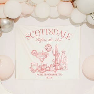 Puede incluir: Una pancarta color crema con texto e ilustraciones en rosa, incluyendo una margarita, un cactus y una botella de tequila. La pancarta dice "SCOTTSDALE Before the Veil" y "KATIE'S BACHELORETTE 2024". Globos blancos y plateados rodean la pancarta.