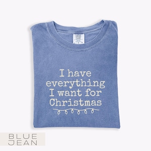May include: A blue t-shirt with the text "I have everything I want for Christmas" in white. The shirt has a crew neck and a tag that says "Comfort Colors". The bottom of the shirt has a string of lights.