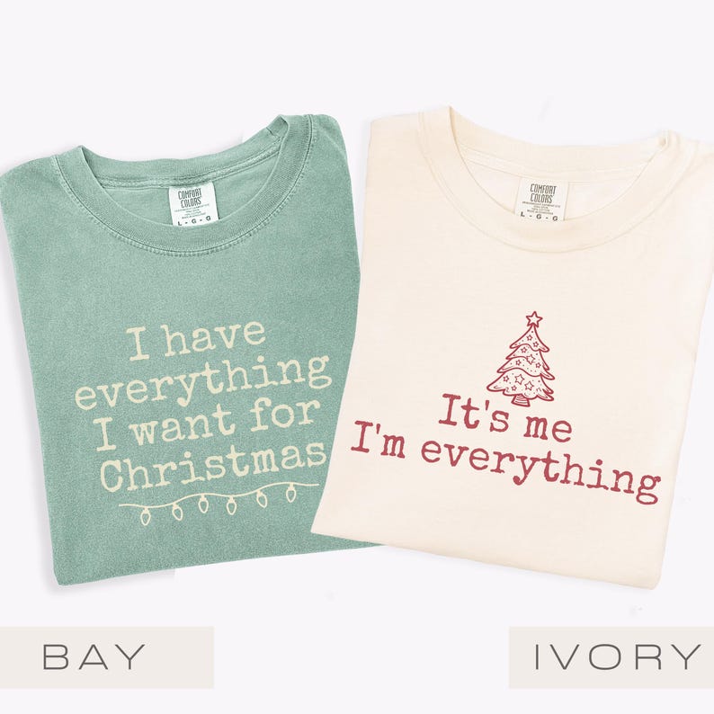 May include: Two t-shirts, one in bay green and one in ivory, with festive text. The bay green shirt reads "I have everything I want for Christmas" with fairy lights. The ivory shirt says "It's me I'm everything" with a Christmas tree design.