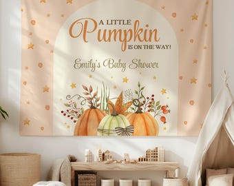 May include: A peach-coloured backdrop with gold stars and a white archway. The text "A Little Pumpkin is on the Way!" is written in a brown script font. Below the text is "Emily's Baby Shower" in a smaller font. Three pumpkins with autumn leaves and berries are at the bottom of the archway.