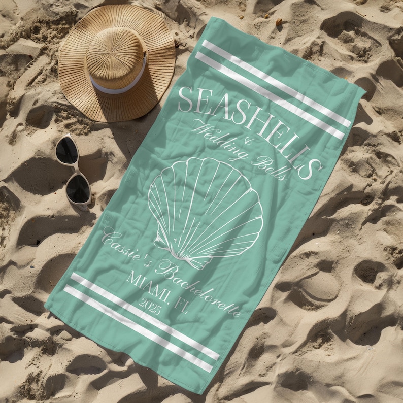 May include: A turquoise beach towel with white stripes and the text "Seashells & Wedding Bells Cassie's Bachelorette Miami, FL 2025". A white seashell graphic is in the centre of the towel.