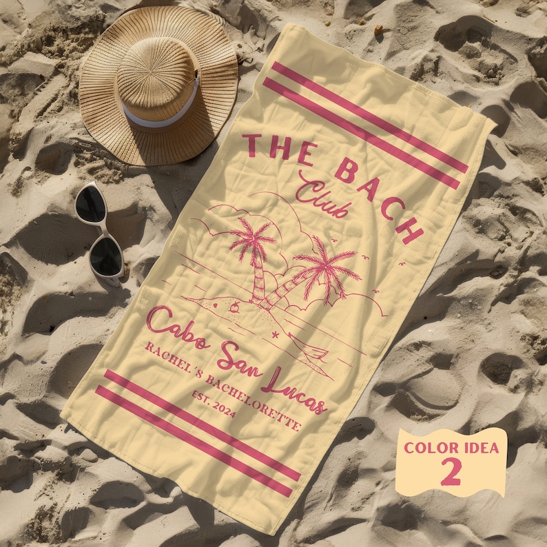 May include: A yellow beach towel with pink text that reads "THE BACH Club Cabo San Lucas Rachel's Bachelorette Est. 2024". The towel features a pink illustration of palm trees and a beach scene. The text "COLOR IDEA 2" is written in pink on a yellow circle in the bottom right corner of the towel.