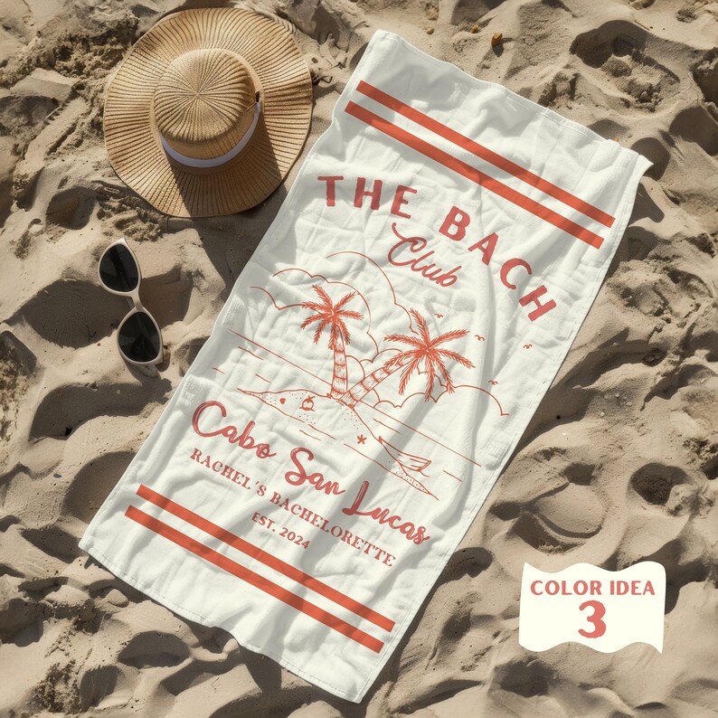 May include: A white beach towel with red text and graphics. The text reads "THE BACH Club Cabo San Lucas Rachel's Bachelorette Est. 2024". The graphic is of two palm trees on a beach.