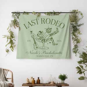Pu&ograve; includere: Un arazzo verde con il testo "Last Rodeo" e una silhouette di una cowgirl in un bicchiere da martini. Il testo "Nicole's Bachelorette" &egrave; sotto l'immagine, con la posizione "Nashville, TN". Il testo "Est. 2024" &egrave; sul lato destro dell'immagine.