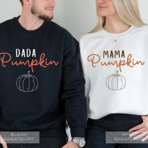 Pu&ograve; includere: Una coppia indossa felpe abbinate nere e bianche con il testo "Dada Pumpkin" e "Mama Pumpkin" in lettere arancioni. Ogni felpa presenta un semplice disegno di una zucca.